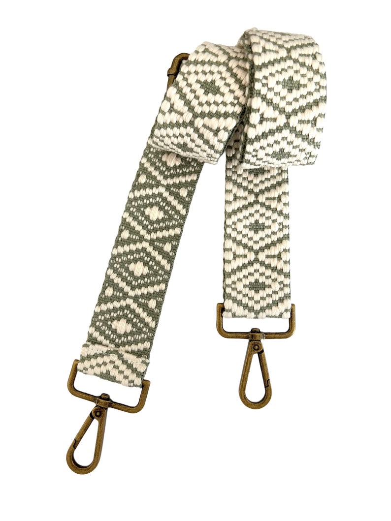 Op de afbeelding: Een geweven band met een groen en wit patroon en messing gespen. De band is ongeveer 122 cm lang.