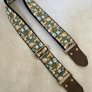 May include: A green, white and orange floral guitar strap with brown leather ends and gold metal buckles.