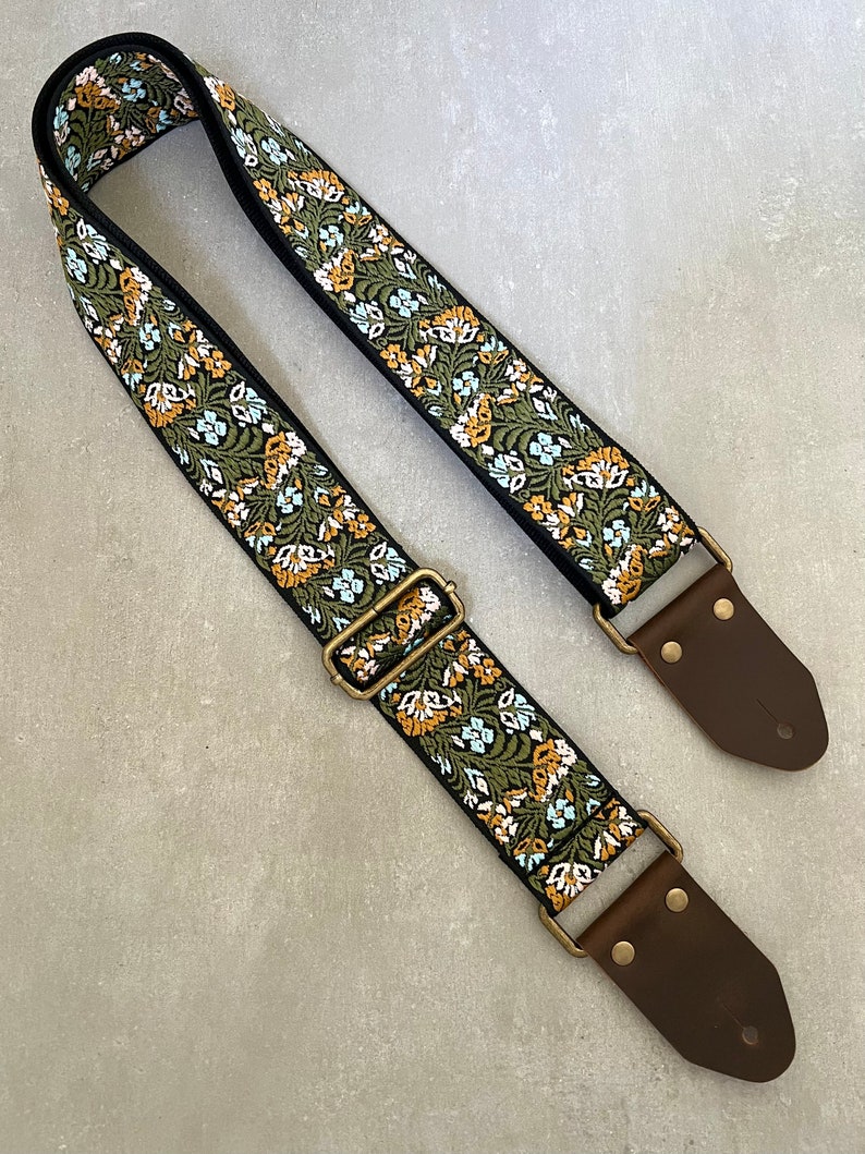 May include: A green, white and orange floral guitar strap with brown leather ends and gold metal buckles.