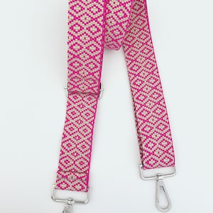 Op de afbeelding: Een geweven band in roze en beige met zilveren draaibare gespen. De band is ongeveer 2,5 cm breed.