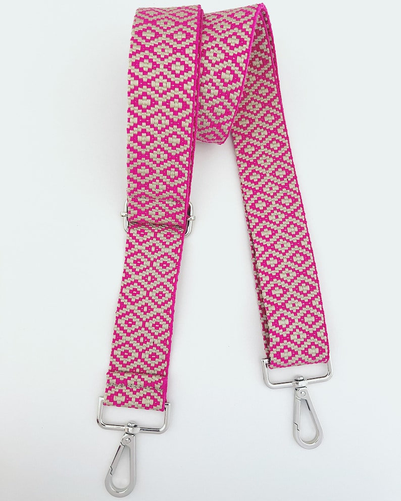 Op de afbeelding: Een geweven band in roze en beige met zilveren draaibare gespen. De band is ongeveer 2,5 cm breed.
