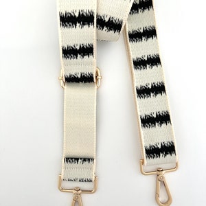 Op de afbeelding: Een verstelbare band met gouden hardware, met een wit en zwart gestreept ontwerp met een ikat-patroon.