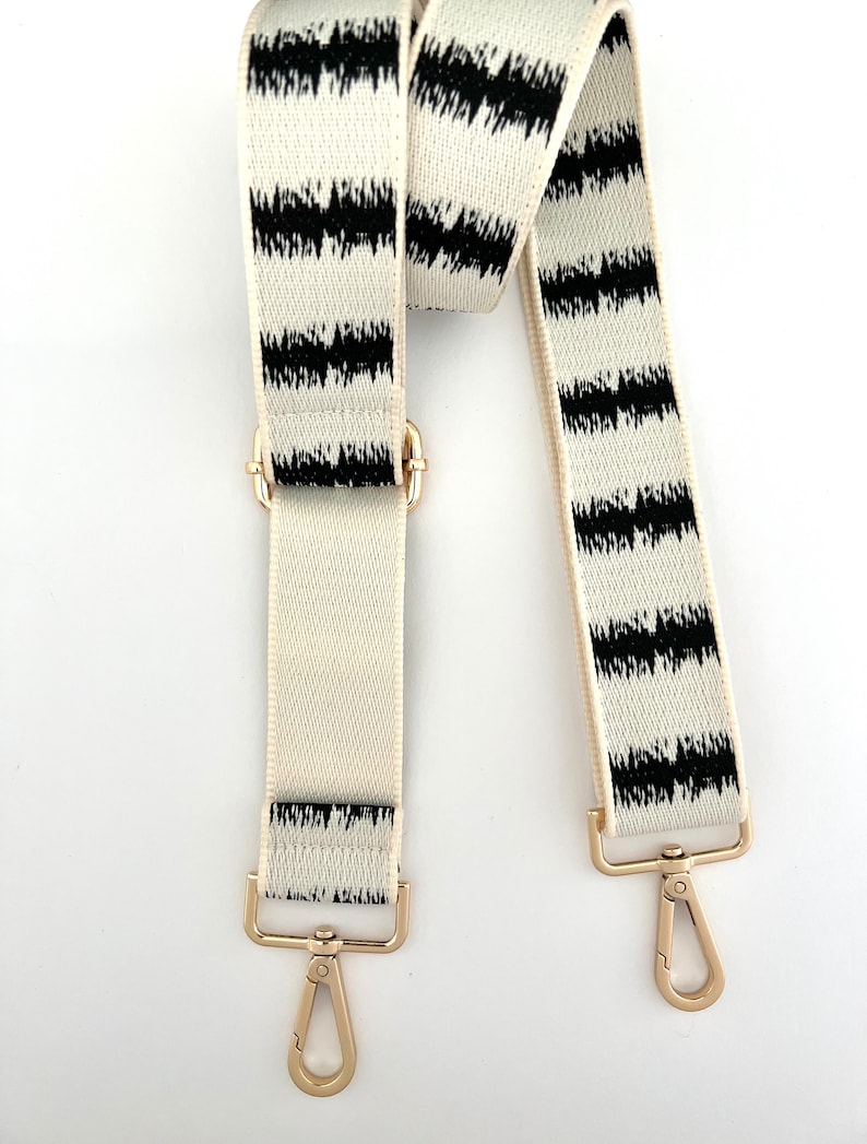 Op de afbeelding: Een verstelbare band met gouden hardware, met een wit en zwart gestreept ontwerp met een ikat-patroon.
