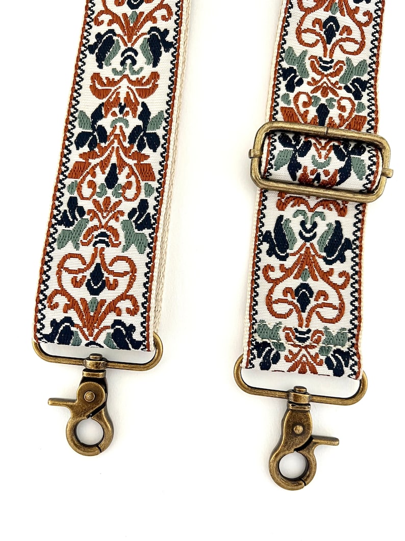 May include: A replacement bag strap featuring a woven pattern in rust orange, sage green, and navy blue on a cream background. The strap includes antique brass-toned metal swivel lobster clasps and an adjustable sliding buckle for length control.