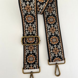 May include: A black and brown woven guitar strap with a floral pattern and gold metal clasps.