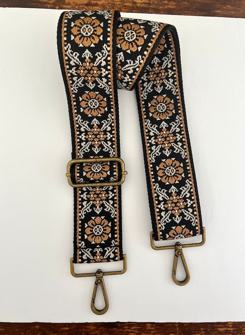 May include: A black and brown woven guitar strap with a floral pattern and gold metal clasps.