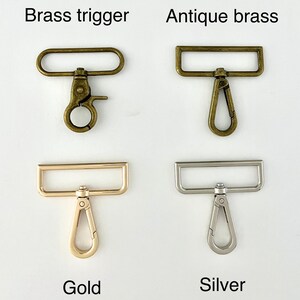 May include: Four metal swivel snap hooks with rectangular loops. Top left is labelled Brass trigger, top right is Antique brass, bottom left is Gold, and bottom right is Silver. Each hook features a spring-loaded gate and a rotating swivel base.