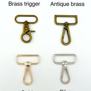Op de afbeelding: Vier verschillende soorten triggergespen, waaronder messing trigger, antiek messing, goud en zilver. Elke gesp heeft een rechthoekige bovenste balk en een haak.