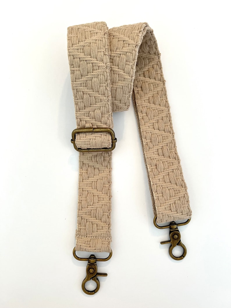 Op de afbeelding: Een beige geweven band met twee gouden metalen gespen en een gouden metalen gesp.