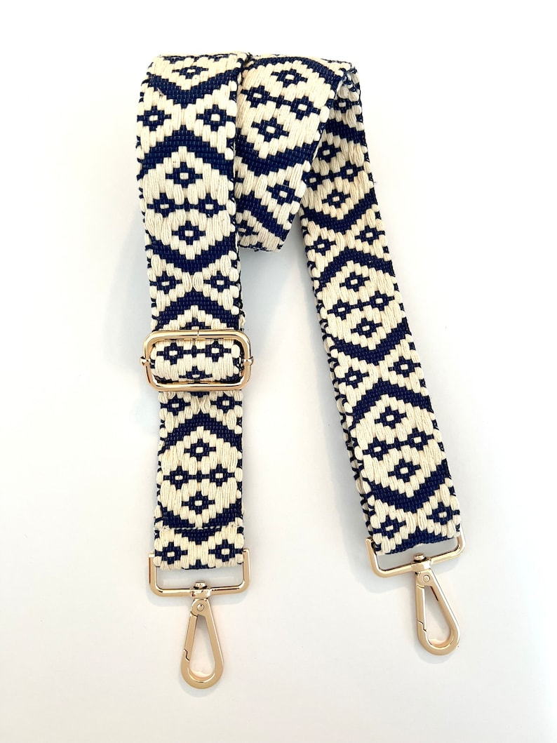 Op de afbeelding: Een verstelbare band met een wit en marineblauw geometrisch patroon en gouden hardware. De band is geschikt voor tassen of handtassen.