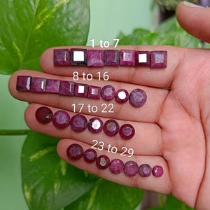 May include: A hand displays a collection of faceted, deep red gemstones. The gemstones are arranged in rows, with the text "1 to 7", "8 to 16", "17 to 22", and "23 to 29" labeling each row. The gemstones vary in shape and size.