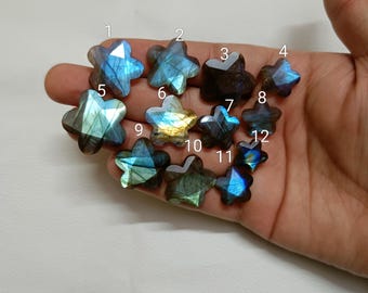 May include: A collection of twelve star-shaped labradorite gemstones, each displaying iridescent blue, green, and gold flashes. The gemstones vary in size and are held in a hand, showcasing their unique patterns and colors. These polished stones are ideal for jewelry making or collecting.