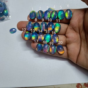 以下が含まれることがあります： 手の上に、1から20まで番号が付けられた20個の虹色の楕円形の宝石が並んでいます。宝石は青、緑、黄色の混合です。