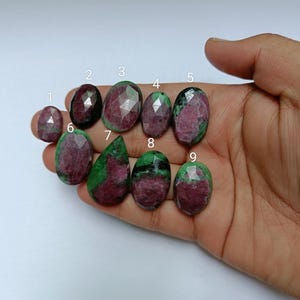 May include: Nine green and pink gemstone cabochons, numbered 1 through 9, are displayed on a hand. The gemstones are oval shaped and have a faceted cut.