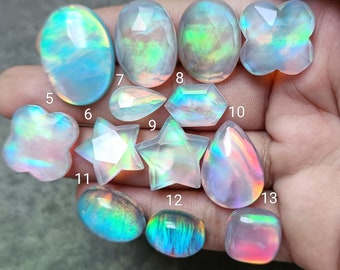 May include: Thirteen iridescent opal gemstones of various shapes and sizes, including oval, teardrop, star, and flower shapes. The gemstones are arranged on a hand, with numbers 1 through 13 written next to each stone.