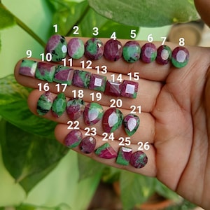 Könnte beinhalten: Sechsundzwanzig grüne und rosafarbene Edelsteine, nummeriert von 1 bis 26, werden auf einer Hand gezeigt. Die Edelsteine sind in verschiedenen Formen und Größen.