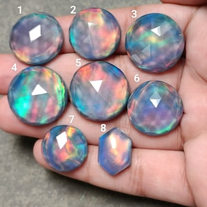 Op de afbeelding: Acht iriserende edelsteen-cabochons in verschillende tinten paars, blauw en roze met een gefacetteerde, afgeronde vorm.