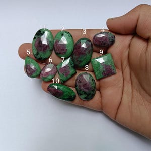 May include: Ten green and pink gemstones of various shapes and sizes. The gemstones are arranged in a hand.