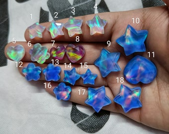 May include: A hand holding 18 iridescent glass cabochons in various shapes, including stars, hearts, and flowers. The cabochons are numbered 1 through 18.