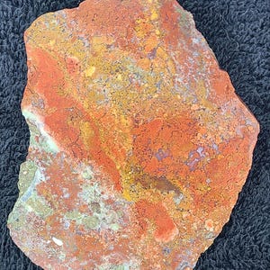 May include: A natural, irregularly shaped stone with a vibrant mix of colors. The surface displays a blend of red, orange, yellow, and hints of green and purple. The stone's texture appears rough and organic.
