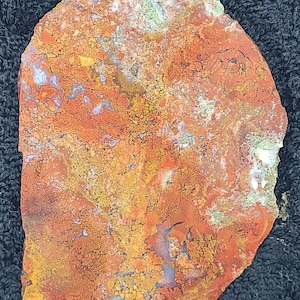 May include: A polished, irregularly shaped stone slab with a vibrant color palette. The surface displays a mix of orange, yellow, and red hues, with hints of green and white. The stone's texture appears rough and natural, showcasing its unique mineral patterns.