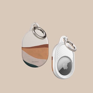 Könnte beinhalten: Zwei AirTag-Schlüsselanhänger, einer mit weißem Hintergrund und einem abstrakten Design in Braun, Weiß und Grün mit dem Text "SALAVISA" und der andere mit weißem Hintergrund und einem silbernen Apple-Logo.