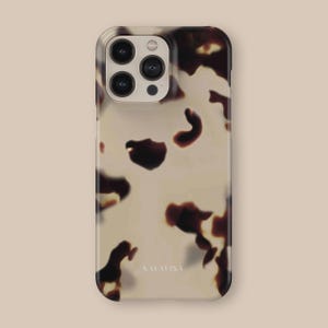 May include: A white and brown tortoiseshell iPhone case with a black camera lens and the word "SALAVISA" printed on the back.