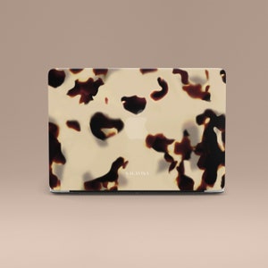 Puede incluir: Un ordenador portátil con un patrón de caparazón de tortuga en la tapa. El portátil tiene un borde negro y el logotipo de Apple es visible en la tapa. El texto "SALAVISA" está impreso en la parte inferior de la tapa.