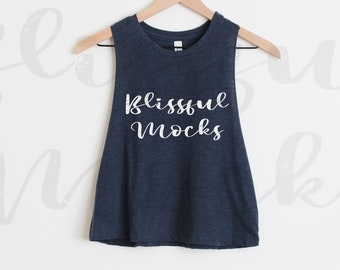 May include: A navy blue sleeveless tank top hanging on a wooden hanger. The tank top has the words "Blissful Mocks" printed in white script across the front. The background is a plain white wall.