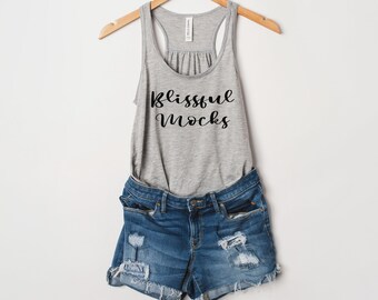 May include: A gray tank top with the text "Blissful Mocks" printed on the front. The tank top is hanging on a wooden hanger and is paired with denim shorts.