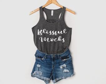 May include: A gray tank top with the text "Blissful Mocks" printed in white. The tank top is hanging on a wooden hanger and is paired with blue denim shorts.