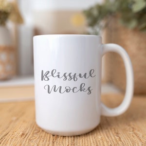 Könnte beinhalten: Eine weiße Keramiktasse mit einer schwarzen, kursiv geschriebenen Aufschrift "blissful mocks".