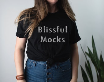 May include: Black t-shirt with the text "Blissful Mocks" in a distressed white font. The shirt is knotted at the waist and paired with blue jeans. A brown leather bracelet is visible on the left wrist.