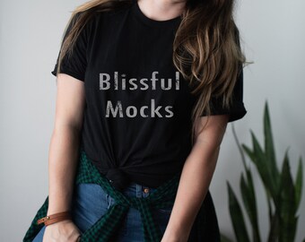 May include: A black t-shirt with the text "Blissful Mocks" printed on the front. The shirt is tied at the waist and worn with a green and black plaid shirt.