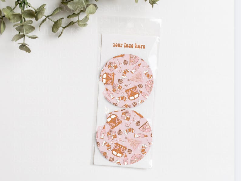 May include: Two pink round coasters with a brown and white pattern of a vintage van, Christmas trees, and other holiday designs. The text "your logo here" is printed on a white card behind the coasters.