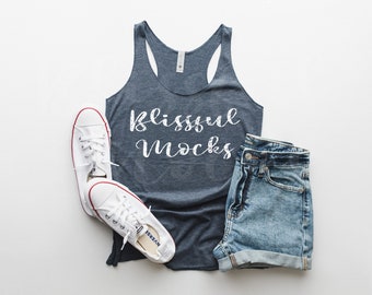 May include: A blue tank top with the text "blissful mocks" printed on the front. The tank top is laying on a white surface with a pair of white sneakers and denim shorts.