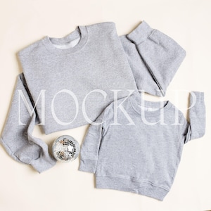 May include: Two grey sweatshirts, one adult-sized and one child-sized, laid out on a cream-coloured background. A silver disco ball is in the centre of the image.