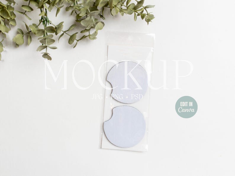 May include: Two white blank round car coasters in a clear plastic package. The package has the text "MOCKUP" and "JPG PNG PSD" printed on it. The text "EDIT IN Canva" is printed on a light blue circle.