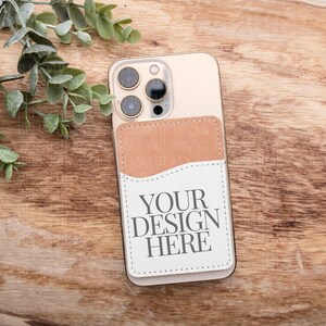 May include: A white phone case with a brown leather pocket on the back. The case has a camera lens cutout and the text "YOUR DESIGN HERE" printed on the pocket.