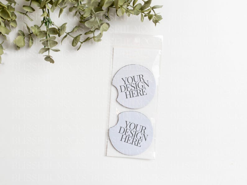 May include: Two white round coasters with a cut-out for a cup. The coasters have the text "YOUR DESIGN HERE" printed on them.