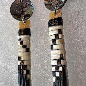 May include: Handmade earrings featuring iridescent abalone shell discs and woven rectangular pendants. The pendants are crafted with alternating black and cream-colored strips, creating a checkered pattern. The earrings hang from silver-colored ear wires.