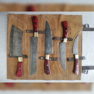 May include: A set of five knives with Damascus steel blades and red and black wooden handles are displayed in a brown leather roll. The roll has a strap and buckle closure.