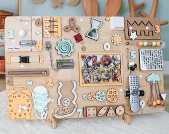 May include: A wooden activity board with various interactive elements for children. Features include a clock, gears, a maze, a light switch, a remote control, and a picture of animals. The board is designed to stimulate sensory and fine motor skills.