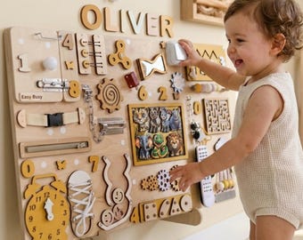 Puede incluir: Un tablero sensorial de madera con varios elementos interactivos, como engranajes, pestillos y un reloj. El nombre "OLIVER" se muestra en la parte superior. Un niño interactúa con el tablero. Diseñado para el desarrollo infantil temprano.