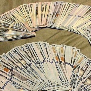May include: Two large fans of United States one hundred dollar bills, fanned out on a textured surface. The bills are crisp and new, with the portrait of Benjamin Franklin visible on each.