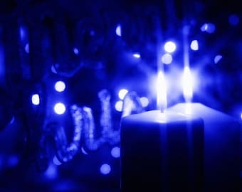 Puede incluir: Una sola vela blanca con una llama azul arde brillantemente sobre un fondo de luces azules bokeh.