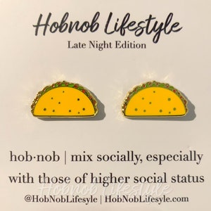 May include: A pair of gold-colored taco earrings with yellow, green, and red details. The earrings are on a white card with the text "Hobnob Lifestyle Late Night Edition" and "hobnob | mix socially, especially with those of higher social status @HobNobLifesyle | HobNobLifesyle.com".