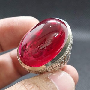 May include: A silver ring with a large, oval-shaped, red gemstone.