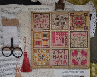 May include: A square cross-stitch sampler featuring nine grid sections with geometric patterns and the text In The Quilt of Life, Friends are The Stitches, That Hold It Together, accompanied by lace trim, thread spools, and small scissors.