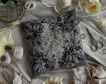 May include: A square, off-white pillow with a black floral lace overlay featuring roses. The pillow is surrounded by cream-colored roses, spools of thread, lace trim, and vintage sewing supplies, including scissors and thread.